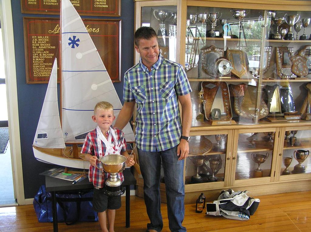Andrew & Cam Brown standing in front of the trophy cabinet at the Wakatere Boating Club with the Wilson & Horton Trophy. Behind them is one of two 1 metre model sunbursts made by Robert Brooke. - 2014 Sunburst Nationals © Nigel Price